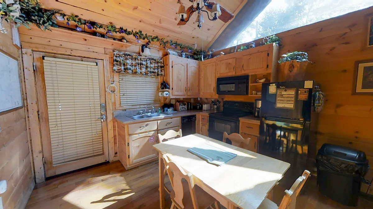 This image highlights a warm, inviting kitchen and dining area. It features wooden cabinets, a four-person dining table set with chairs, modern kitchen appliances, and decorative plants that add a cozy touch. The layout emphasizes both the functional cooking space and the comfortable area for meals and gatherings.