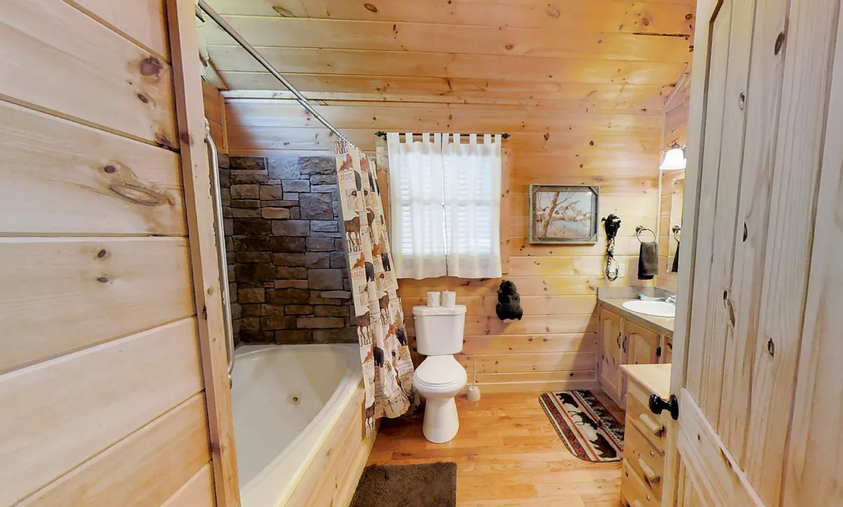 This image features an inviting interior bathroom scene with a bathtub set against a charming stone wall. Wooden cabinetry and decorative accents add warmth, while a window draped with a curtain brings in natural light. The overall feel is cozy and relaxing—a perfect spot to unwind after a busy day exploring local attractions.