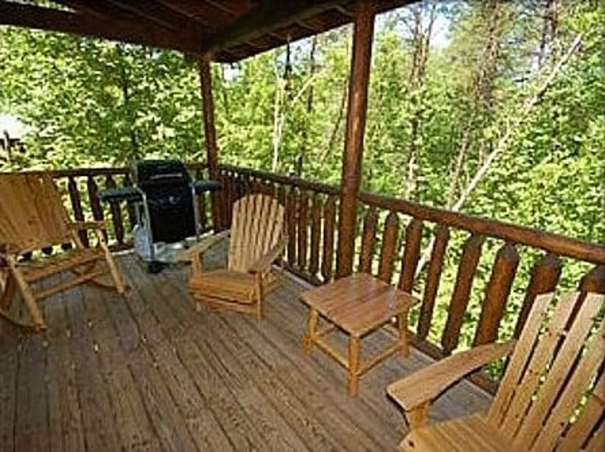 A spacious wooden deck with a BBQ grill and comfortable Adirondack chairs, overlooking natural scenery. The setup is perfect for group gatherings, outdoor meals, and relaxing with a morning coffee or enjoying sunset views.